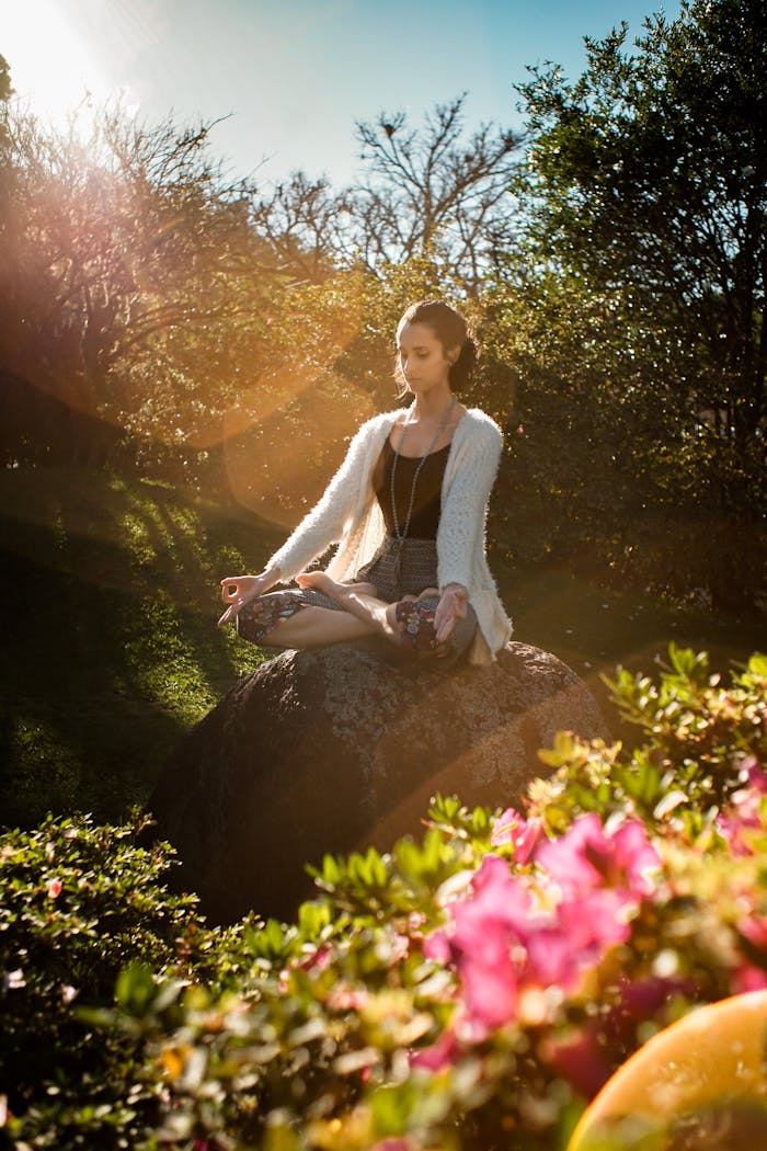 who-we-are Woman in tranquil meditation pose outdoors, bathed in sunlight, surrounded by lush greenery.