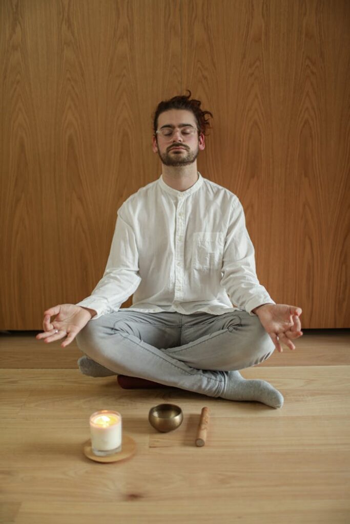 Adult male meditating indoors with a candle and singing bowl, promoting mindfulness and relaxation.